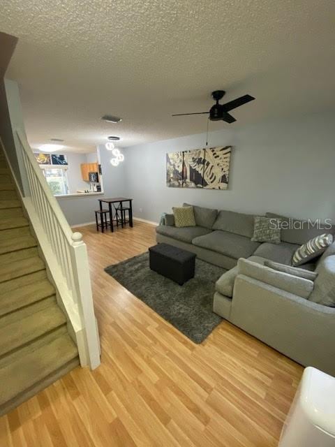 living room featuring ceiling fan, a textured ceiling, and wood-type flooring