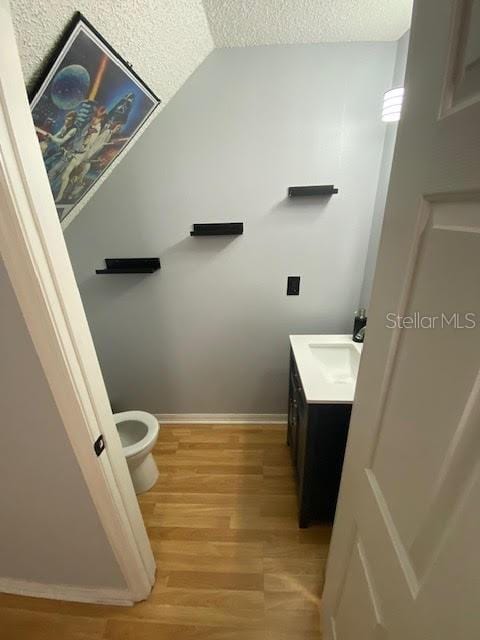 bathroom featuring wood-type flooring, toilet, vanity, and a textured ceiling