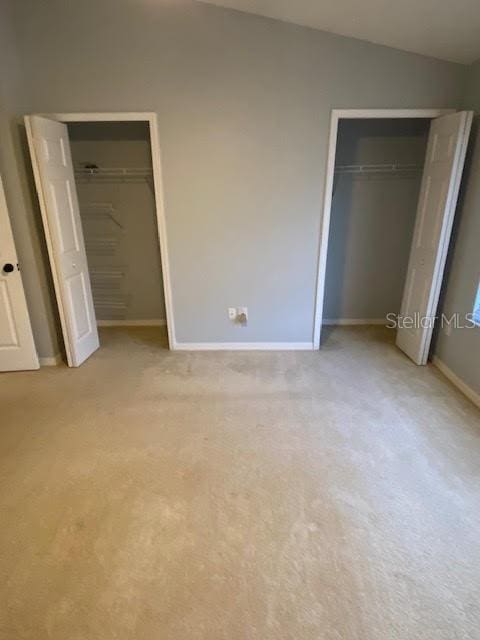 unfurnished bedroom with light colored carpet, two closets, and lofted ceiling