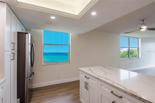 kitchen with stainless steel fridge, ceiling fan, light stone countertops, white cabinets, and light wood-type flooring