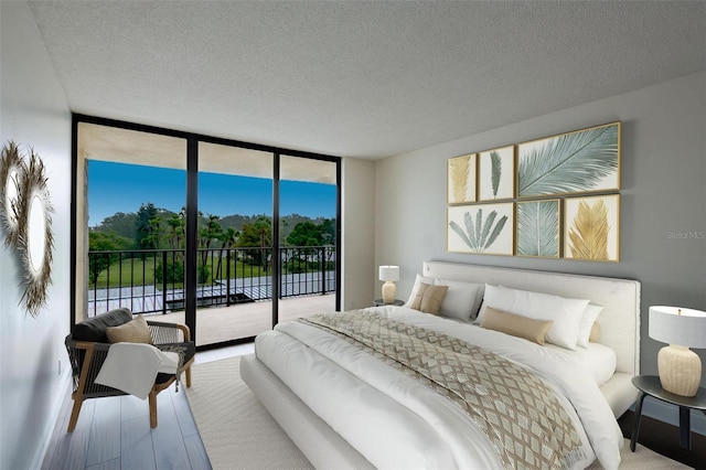 bedroom with expansive windows, access to exterior, a textured ceiling, and hardwood / wood-style flooring