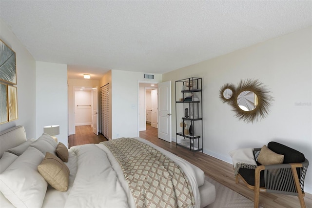 bedroom featuring connected bathroom, hardwood / wood-style floors, a closet, and a textured ceiling