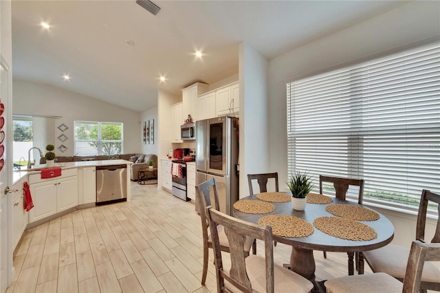 dining space with vaulted ceiling, plenty of natural light, sink, and light hardwood / wood-style flooring