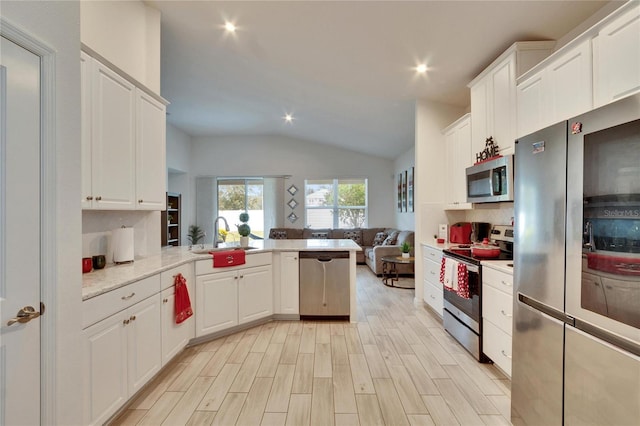 kitchen with stainless steel appliances, vaulted ceiling, sink, and white cabinets