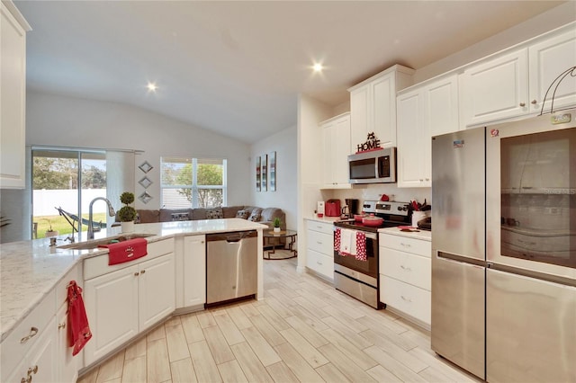 kitchen featuring vaulted ceiling, white cabinetry, sink, stainless steel appliances, and light stone countertops