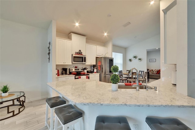 kitchen featuring sink, a breakfast bar area, white cabinets, kitchen peninsula, and stainless steel appliances