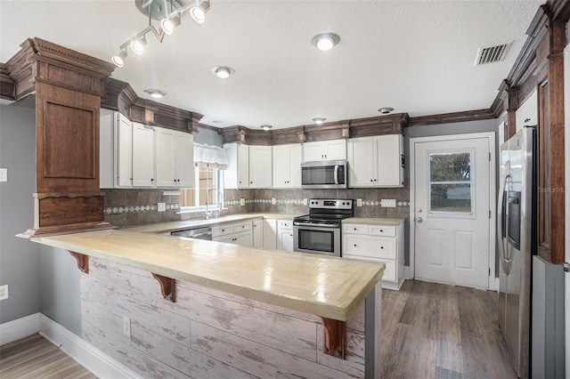 kitchen with dark hardwood / wood-style floors, white cabinets, kitchen peninsula, stainless steel appliances, and crown molding