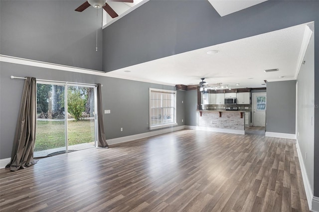 unfurnished living room featuring hardwood / wood-style floors, a towering ceiling, a wealth of natural light, and ceiling fan