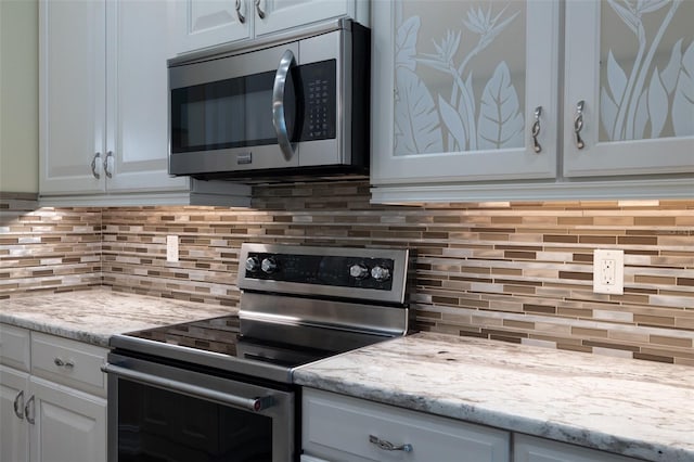 kitchen with white cabinetry, appliances with stainless steel finishes, light stone counters, and decorative backsplash