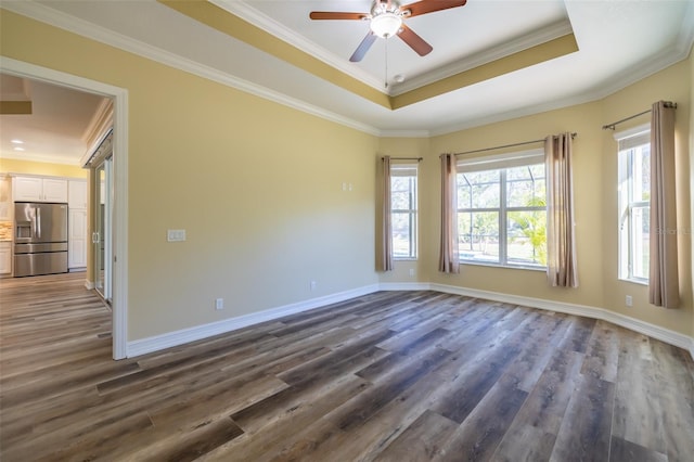 spare room with dark wood-type flooring, ceiling fan, crown molding, and a raised ceiling