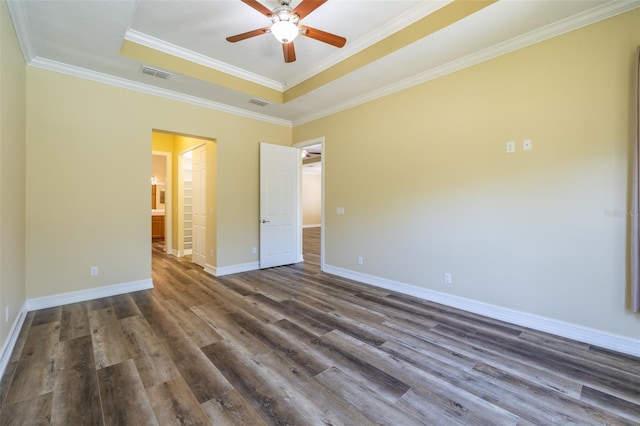 empty room featuring a raised ceiling, ornamental molding, dark wood-type flooring, and ceiling fan