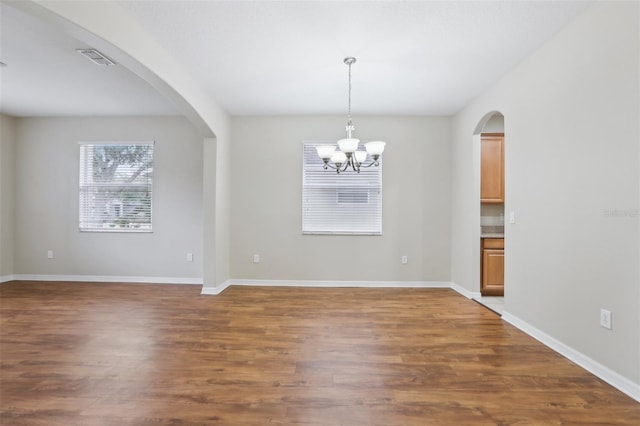 spare room featuring an inviting chandelier and dark hardwood / wood-style floors