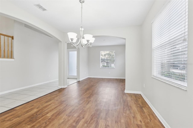 spare room with an inviting chandelier, hardwood / wood-style flooring, and a wealth of natural light