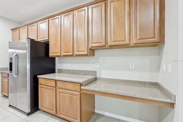 kitchen with built in desk, stainless steel fridge, light stone countertops, and light tile patterned flooring