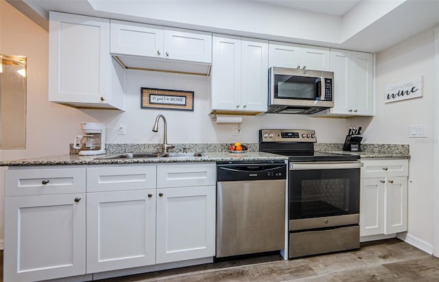 kitchen with sink, stainless steel appliances, light stone counters, light hardwood / wood-style floors, and white cabinets