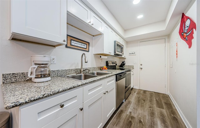 kitchen with appliances with stainless steel finishes, sink, white cabinets, light hardwood / wood-style floors, and light stone countertops