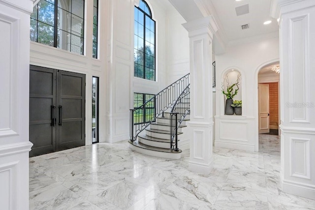 foyer with a towering ceiling, ornamental molding, and decorative columns