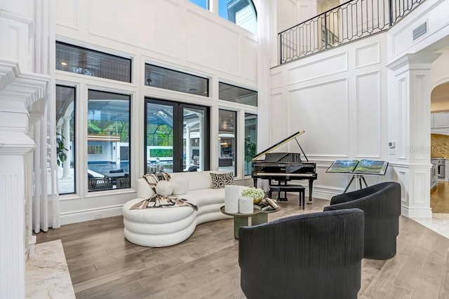 living room with a towering ceiling, light hardwood / wood-style flooring, french doors, and ornate columns