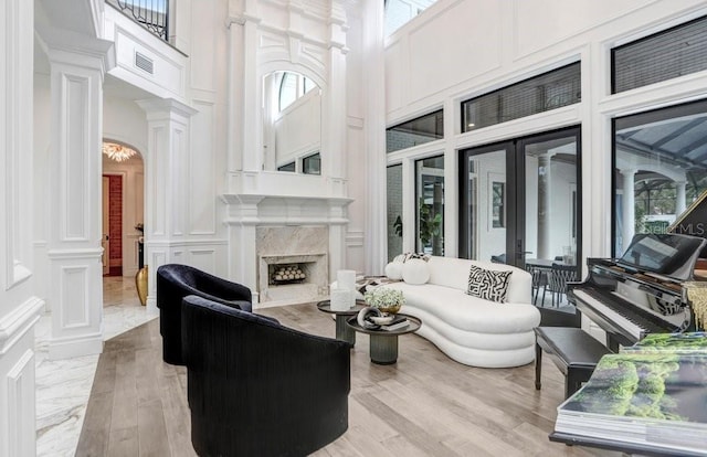 living room featuring light hardwood / wood-style flooring, a towering ceiling, decorative columns, a fireplace, and french doors