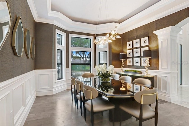 dining room with hardwood / wood-style flooring, ornamental molding, a notable chandelier, and ornate columns