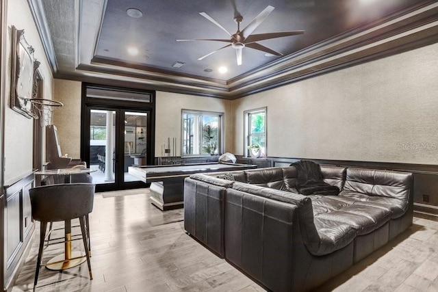 home theater with crown molding, light hardwood / wood-style flooring, a raised ceiling, and french doors