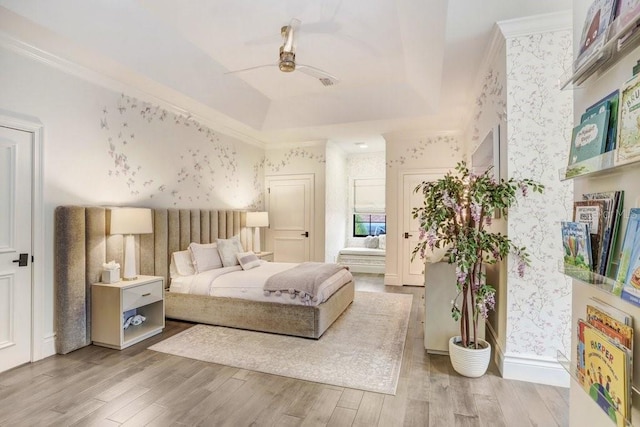 bedroom with crown molding, light hardwood / wood-style floors, ceiling fan, and a tray ceiling