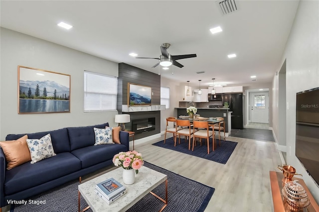 living room with a healthy amount of sunlight, a ceiling fan, visible vents, light wood finished floors, and a large fireplace