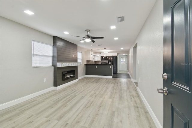 unfurnished living room with baseboards, visible vents, a fireplace, ceiling fan, and light wood-type flooring