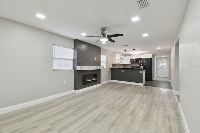 unfurnished living room featuring a large fireplace, ceiling fan, and light wood-type flooring