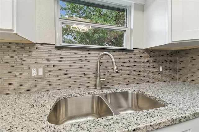 room details featuring white cabinetry, sink, decorative backsplash, and light stone counters