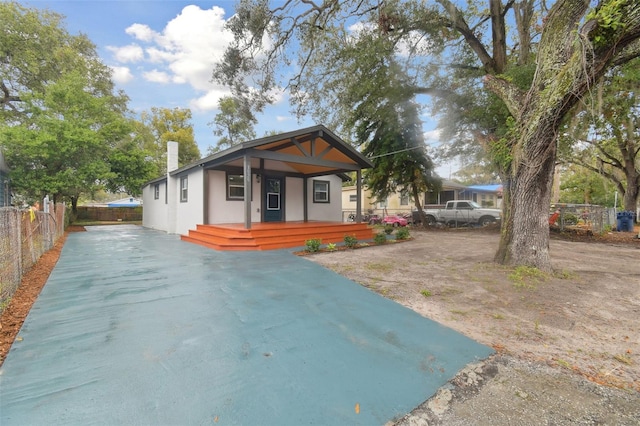 view of front of property featuring stucco siding, covered porch, a chimney, and fence