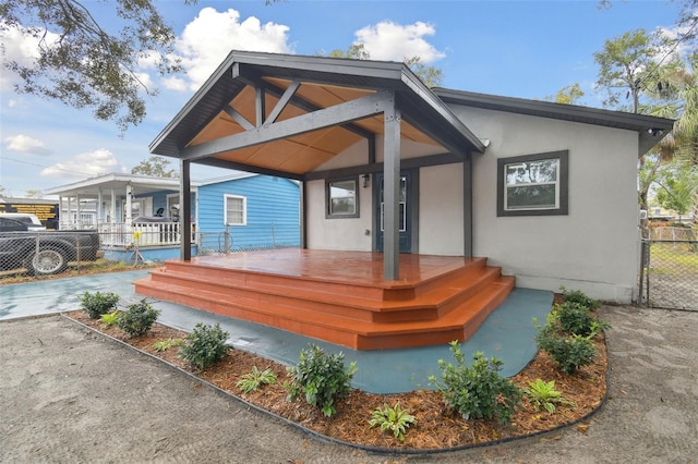 rear view of property featuring fence, covered porch, and stucco siding