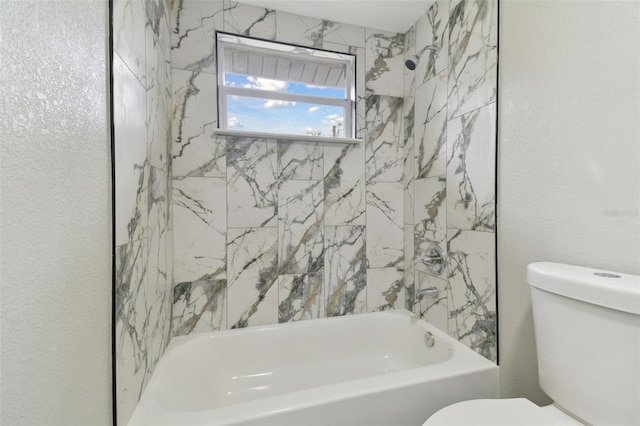 bathroom with tub / shower combination, toilet, and a textured wall