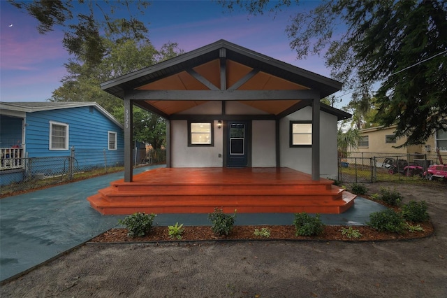 view of front of house with stucco siding, a porch, and fence