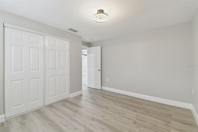 unfurnished bedroom with baseboards, visible vents, wood finished floors, and a closet