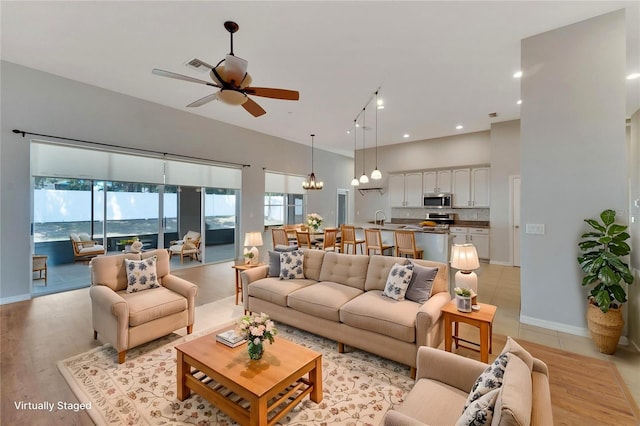 living room featuring sink, ceiling fan with notable chandelier, a high ceiling, and a water view