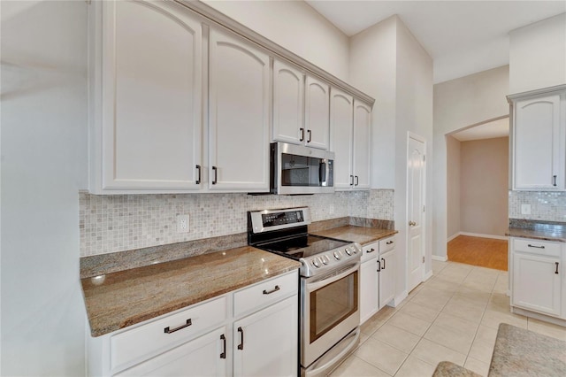 kitchen featuring light tile patterned flooring, appliances with stainless steel finishes, white cabinetry, decorative backsplash, and dark stone counters