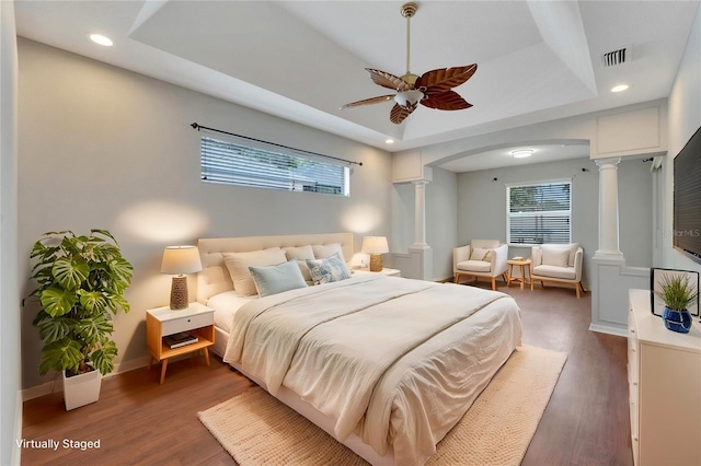 bedroom featuring a tray ceiling, decorative columns, dark hardwood / wood-style floors, and ceiling fan