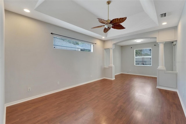 unfurnished living room with hardwood / wood-style floors, a tray ceiling, ceiling fan, and ornate columns