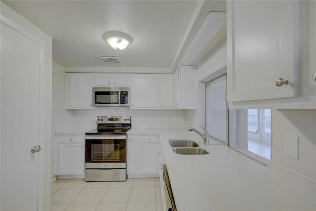 kitchen with appliances with stainless steel finishes, sink, light tile patterned floors, and white cabinets