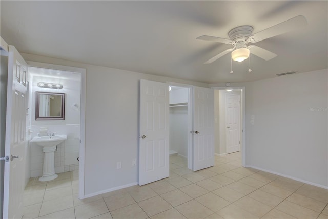 unfurnished bedroom featuring light tile patterned floors, ceiling fan, connected bathroom, a spacious closet, and a closet