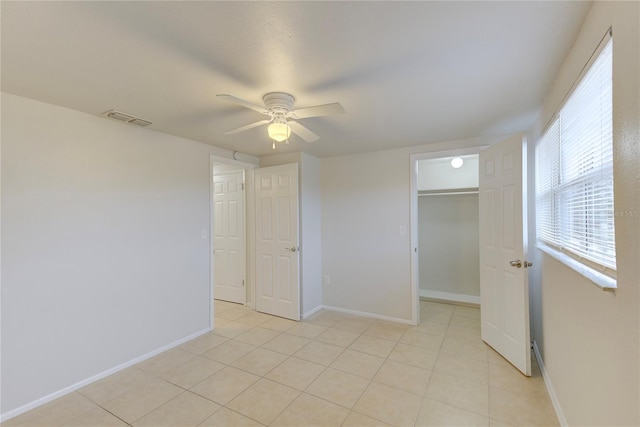 unfurnished bedroom with a walk in closet, light tile patterned floors, ceiling fan, and a closet