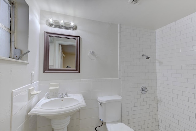 bathroom with sink, tiled shower, tile walls, and toilet