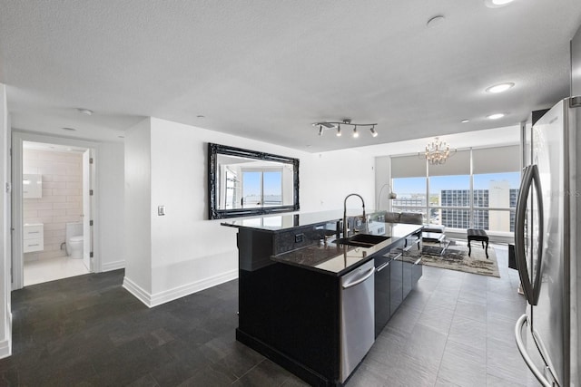 kitchen with dark countertops, appliances with stainless steel finishes, a sink, a textured ceiling, and an island with sink