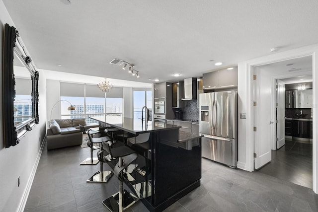 kitchen with backsplash, a kitchen breakfast bar, stainless steel appliances, wall chimney range hood, and a sink