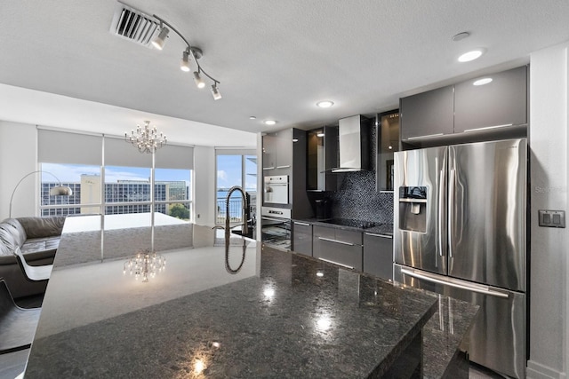 kitchen featuring wall chimney exhaust hood, modern cabinets, visible vents, and stainless steel fridge with ice dispenser