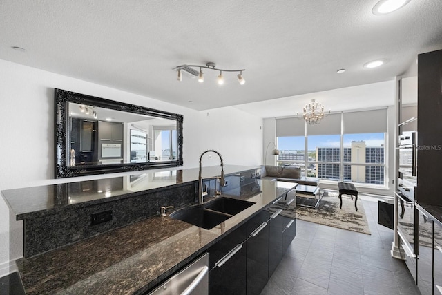 kitchen featuring appliances with stainless steel finishes, dark stone countertops, a textured ceiling, dark cabinetry, and a sink