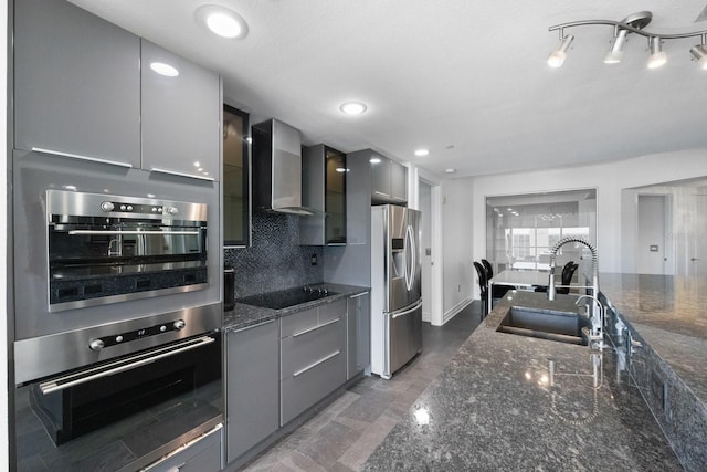 kitchen with stainless steel appliances, a sink, gray cabinets, wall chimney exhaust hood, and tasteful backsplash