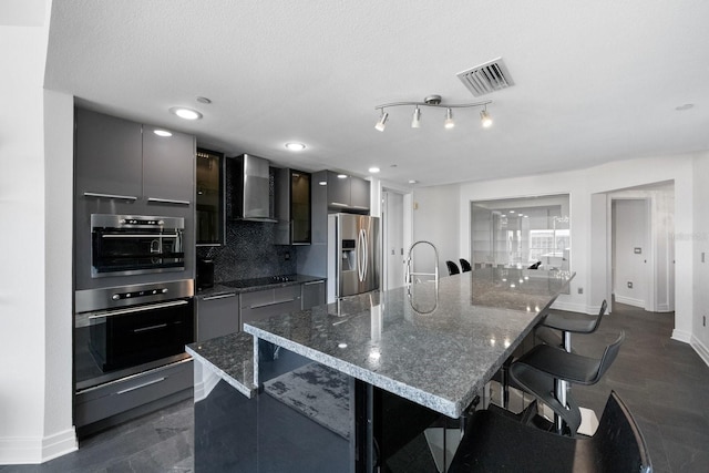 kitchen with visible vents, modern cabinets, a breakfast bar, stainless steel appliances, and wall chimney range hood