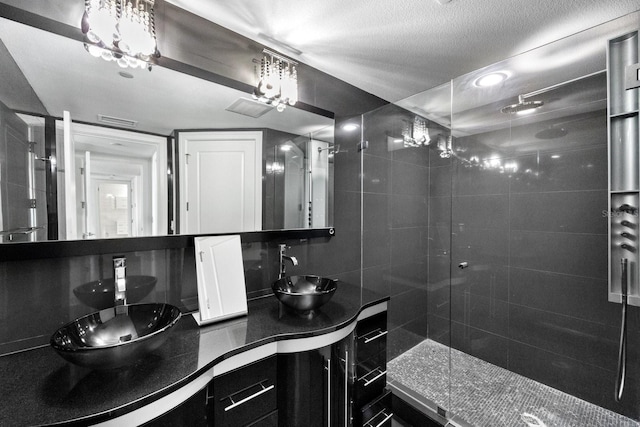 bathroom with double vanity, a sink, a textured ceiling, and a walk in shower